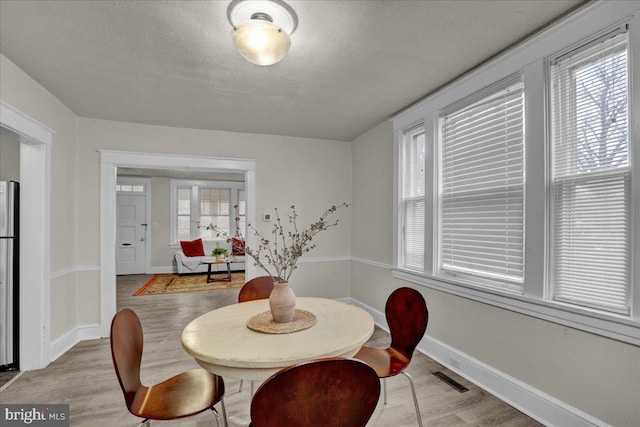 dining area featuring a healthy amount of sunlight, light hardwood / wood-style floors, and a textured ceiling