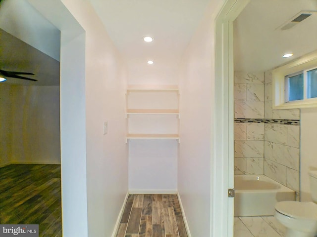 bathroom with hardwood / wood-style flooring, tiled shower / bath, and toilet