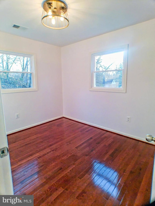 spare room featuring a notable chandelier, wood-type flooring, and a healthy amount of sunlight