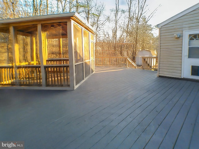 wooden deck with a sunroom and a storage unit