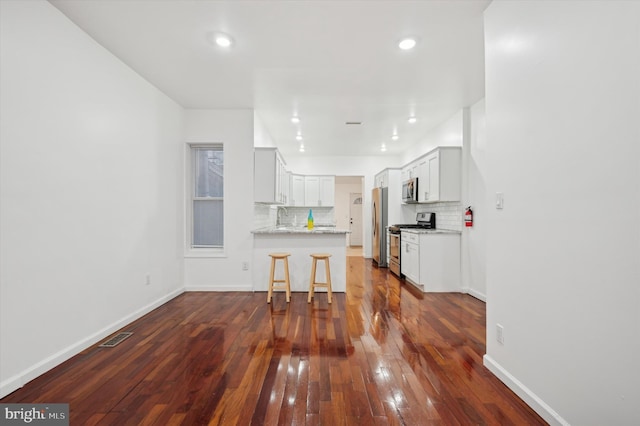 kitchen featuring white cabinetry, appliances with stainless steel finishes, a kitchen bar, and backsplash