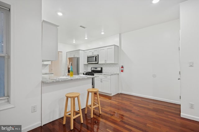 kitchen with appliances with stainless steel finishes, white cabinetry, a kitchen breakfast bar, light stone countertops, and decorative backsplash