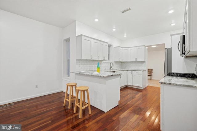 kitchen with dark hardwood / wood-style floors, white cabinetry, backsplash, stainless steel appliances, and light stone countertops