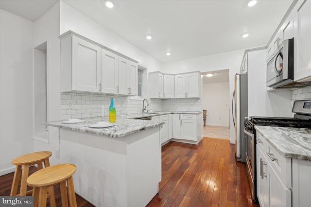 kitchen with white cabinetry, appliances with stainless steel finishes, light stone counters, and a breakfast bar area