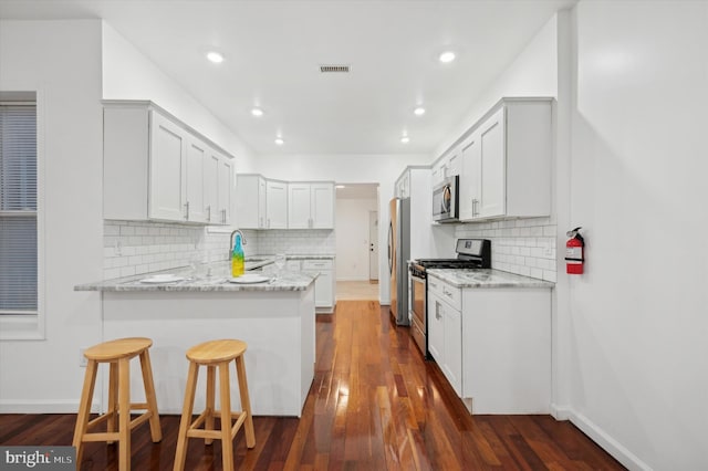 kitchen with light stone counters, stainless steel appliances, kitchen peninsula, and white cabinets