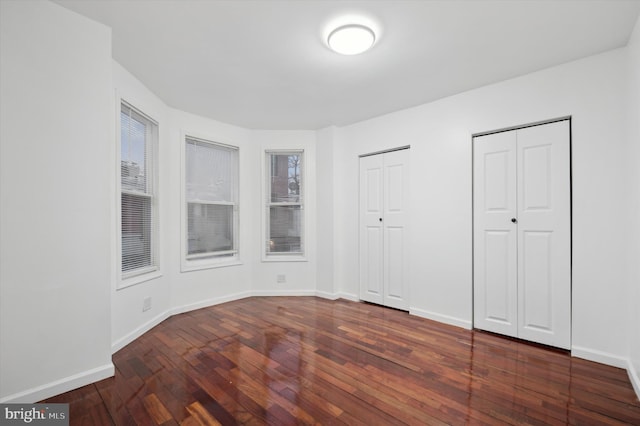 unfurnished bedroom featuring multiple closets and dark hardwood / wood-style flooring