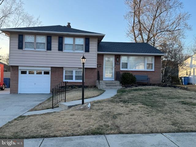 tri-level home with brick siding, concrete driveway, a front yard, a chimney, and an attached garage