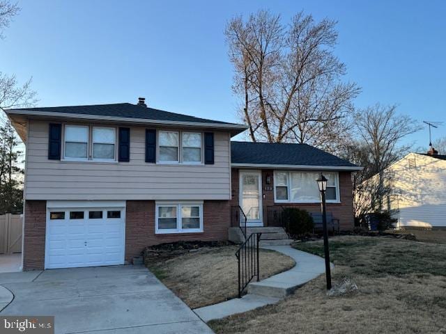 tri-level home with concrete driveway, brick siding, a garage, and a front yard