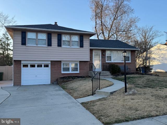 tri-level home featuring brick siding, an attached garage, fence, a front yard, and driveway