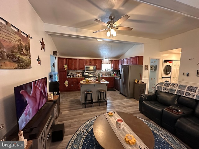 living room featuring lofted ceiling with beams, dark hardwood / wood-style floors, ceiling fan, and stacked washer / dryer