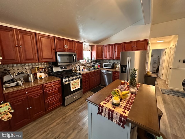 kitchen featuring lofted ceiling, sink, backsplash, stainless steel appliances, and wood-type flooring