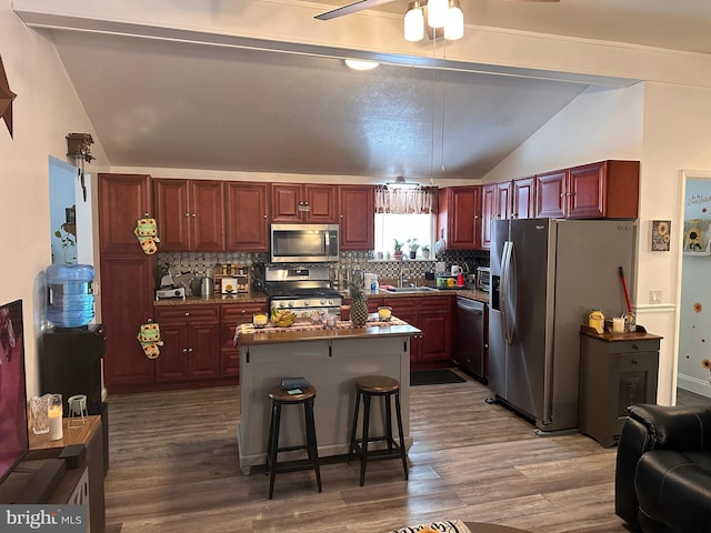 kitchen with a breakfast bar, vaulted ceiling, appliances with stainless steel finishes, a kitchen island, and decorative backsplash