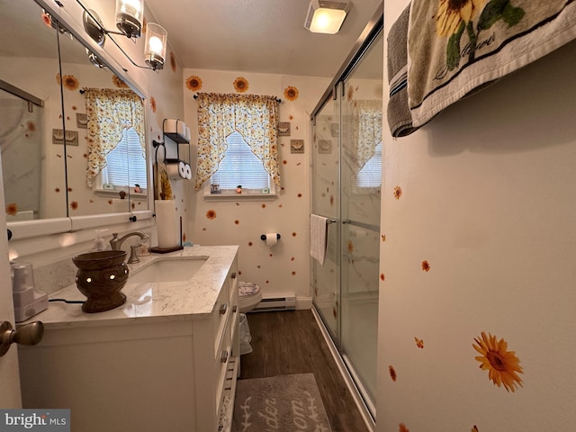 bathroom featuring hardwood / wood-style floors, vanity, a baseboard heating unit, an enclosed shower, and toilet