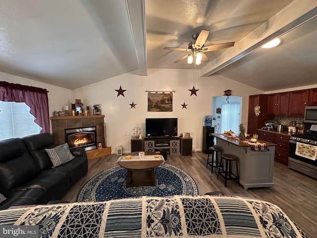 living room with a tiled fireplace, dark wood-type flooring, lofted ceiling with beams, and ceiling fan