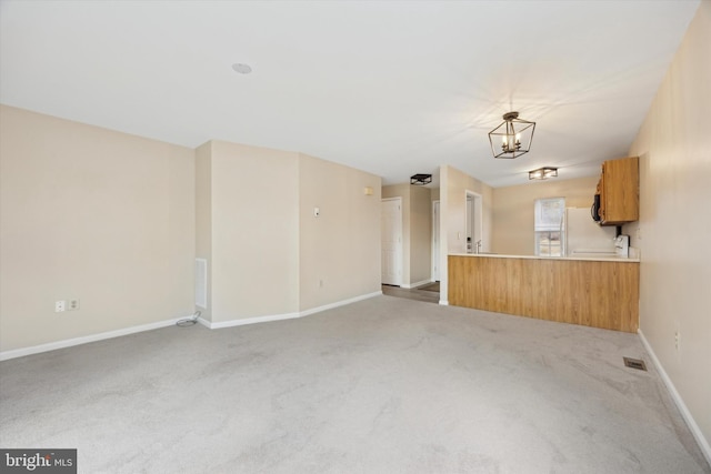 unfurnished living room featuring light carpet and an inviting chandelier