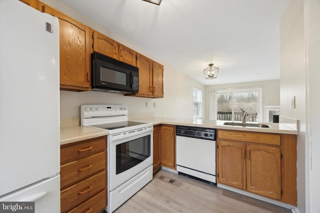 kitchen with sink, kitchen peninsula, white appliances, and light hardwood / wood-style flooring