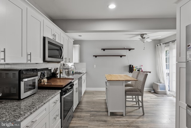 kitchen featuring appliances with stainless steel finishes, tasteful backsplash, wooden counters, white cabinets, and a kitchen breakfast bar