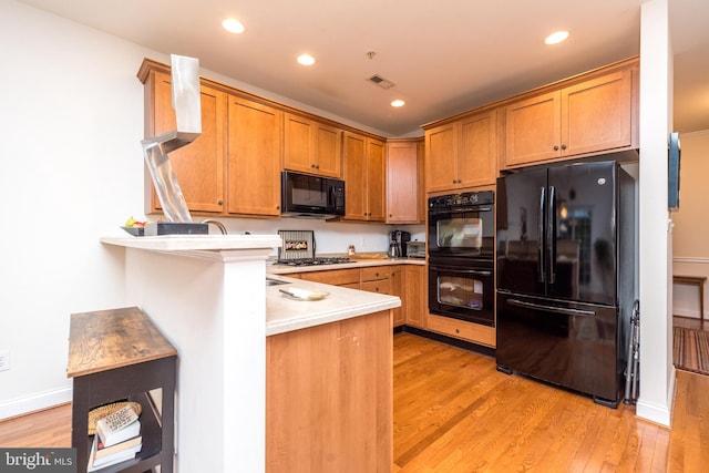 kitchen featuring kitchen peninsula, light wood-type flooring, and black appliances