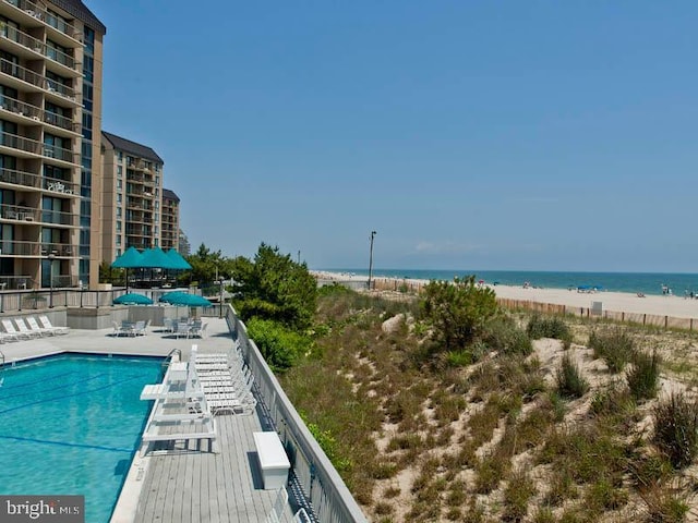 view of swimming pool featuring a water view, a beach view, and a patio area