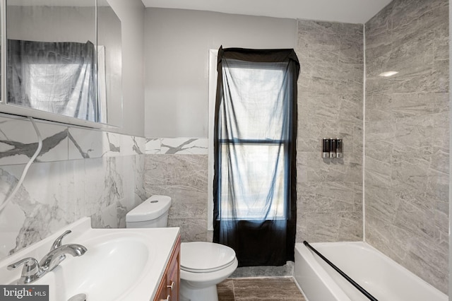 full bathroom with tiled shower / bath, vanity, toilet, and tile walls