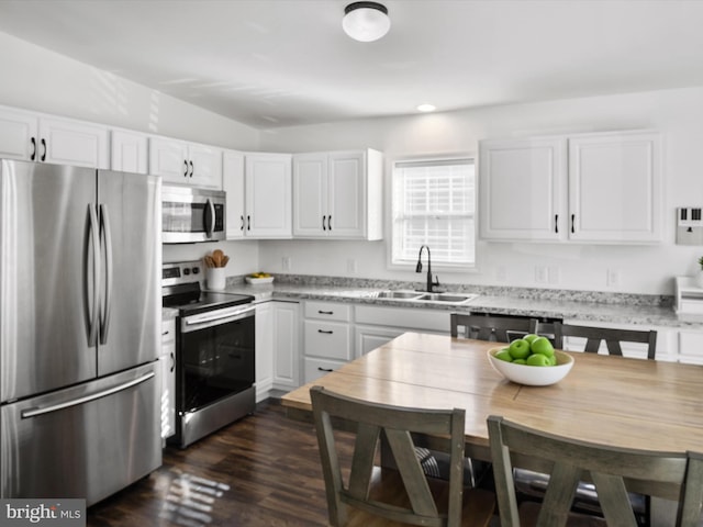 kitchen with sink, white cabinetry, stainless steel appliances, light stone counters, and dark hardwood / wood-style flooring