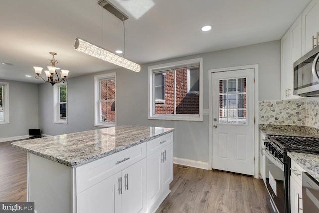 kitchen with hanging light fixtures, stainless steel appliances, white cabinets, a kitchen island, and light wood-type flooring