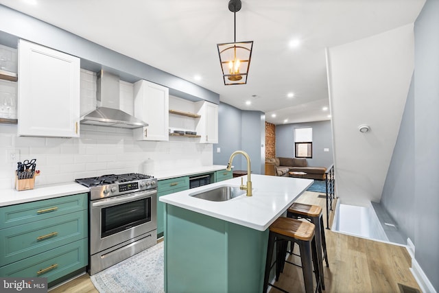 kitchen with sink, stainless steel gas range, white cabinetry, a kitchen island with sink, and wall chimney exhaust hood