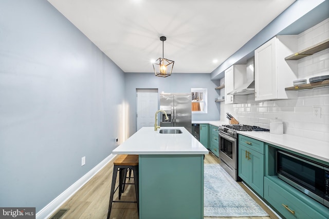 kitchen with appliances with stainless steel finishes, sink, green cabinets, a center island with sink, and wall chimney exhaust hood