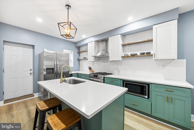 kitchen featuring wall chimney range hood, stainless steel appliances, sink, and a center island with sink