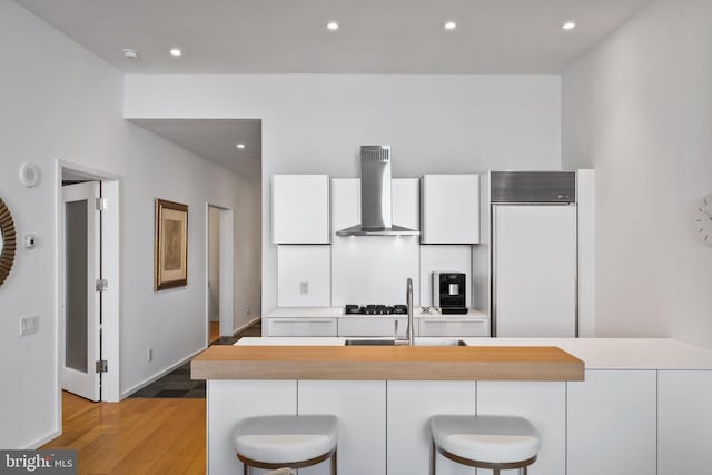 kitchen featuring a breakfast bar, sink, paneled fridge, wall chimney range hood, and white cabinets