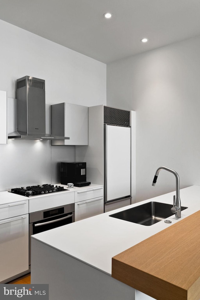 kitchen with sink, wall chimney range hood, black gas cooktop, a center island, and paneled built in fridge