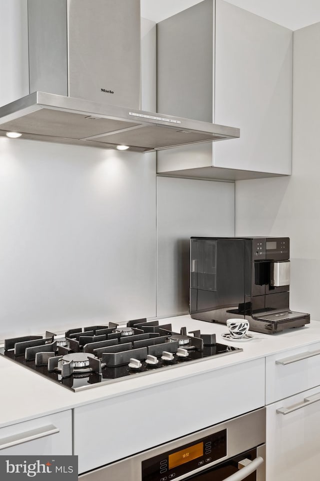 kitchen with white cabinetry, black gas stovetop, stainless steel oven, and wall chimney exhaust hood