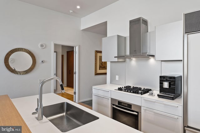 kitchen featuring sink, white cabinets, stainless steel oven, gas cooktop, and wall chimney range hood