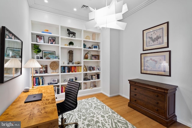 home office with built in shelves, ornamental molding, and light wood-type flooring