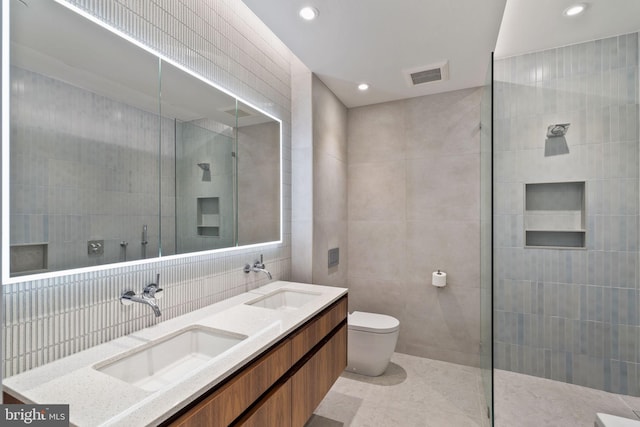 bathroom featuring vanity, tiled shower, tile walls, and toilet