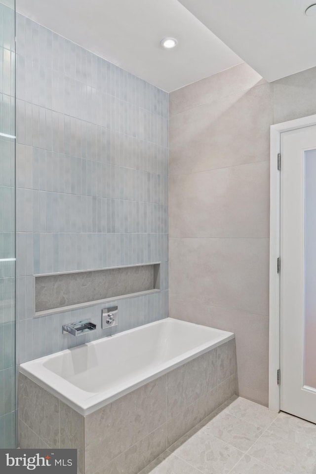 bathroom with tile walls, tile patterned flooring, and tiled bath