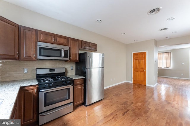 kitchen featuring appliances with stainless steel finishes, backsplash, light stone counters, and light hardwood / wood-style flooring