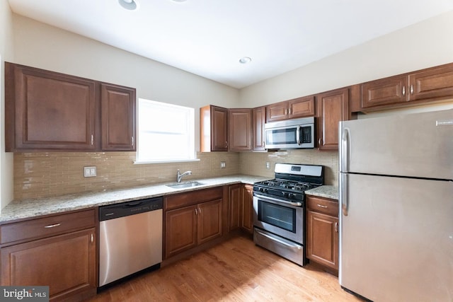 kitchen with stainless steel appliances, light stone countertops, sink, and light hardwood / wood-style floors