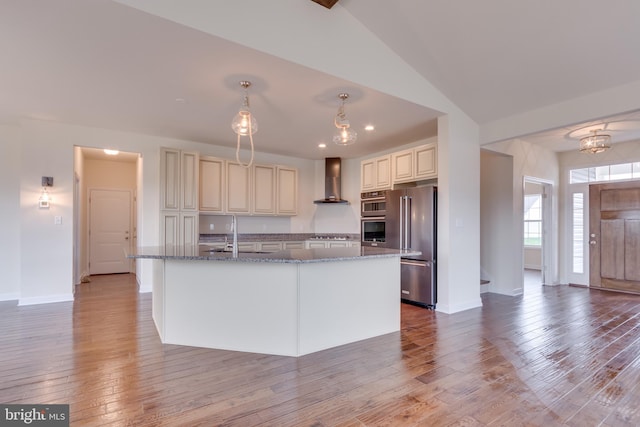 kitchen with decorative light fixtures, a kitchen island with sink, stainless steel appliances, wall chimney range hood, and light wood-type flooring