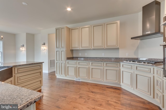 kitchen with stainless steel gas stovetop, light wood-type flooring, cream cabinetry, and wall chimney exhaust hood