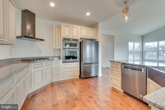 kitchen featuring light hardwood / wood-style flooring, stainless steel appliances, cream cabinets, decorative light fixtures, and wall chimney exhaust hood