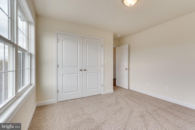 unfurnished bedroom featuring multiple windows, light carpet, and a closet