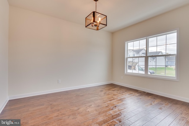 spare room with a notable chandelier and light wood-type flooring