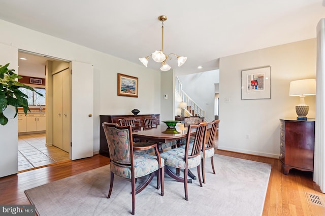 dining room with a chandelier, stairs, visible vents, and light wood-style floors