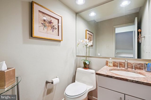 half bathroom featuring recessed lighting, vanity, and toilet