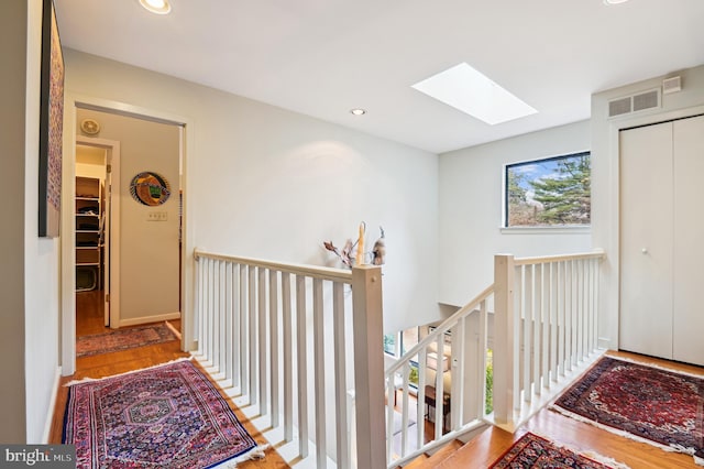 corridor featuring a skylight, visible vents, an upstairs landing, and wood finished floors