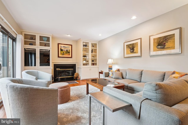 living area featuring a fireplace with flush hearth, recessed lighting, and wood finished floors