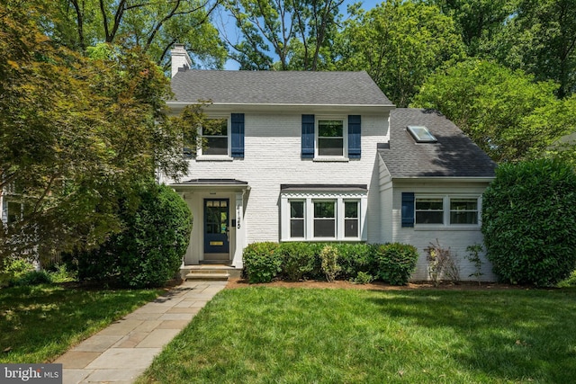 view of front facade featuring a shingled roof, a front yard, brick siding, and a chimney