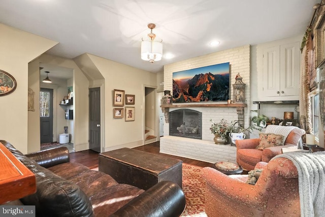 living room with a brick fireplace and dark wood-type flooring