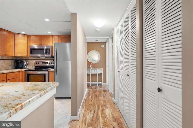 kitchen featuring stainless steel appliances, light stone counters, backsplash, and light hardwood / wood-style floors